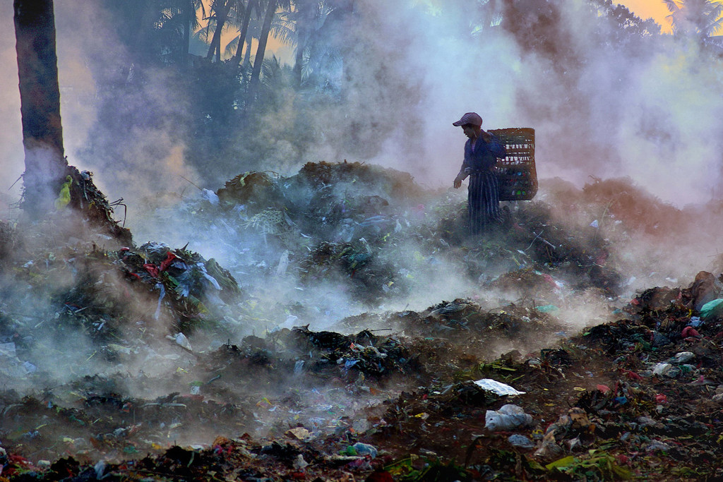 Une fille cherche des matériaux recyclables dans une décharge, au milieu des évaporations de gaz odorant.